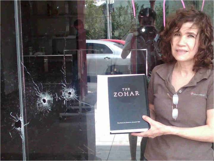 A woman stands with her new Zohar in front of her restaurant, where bullet holes can be seen in the glass – 2011